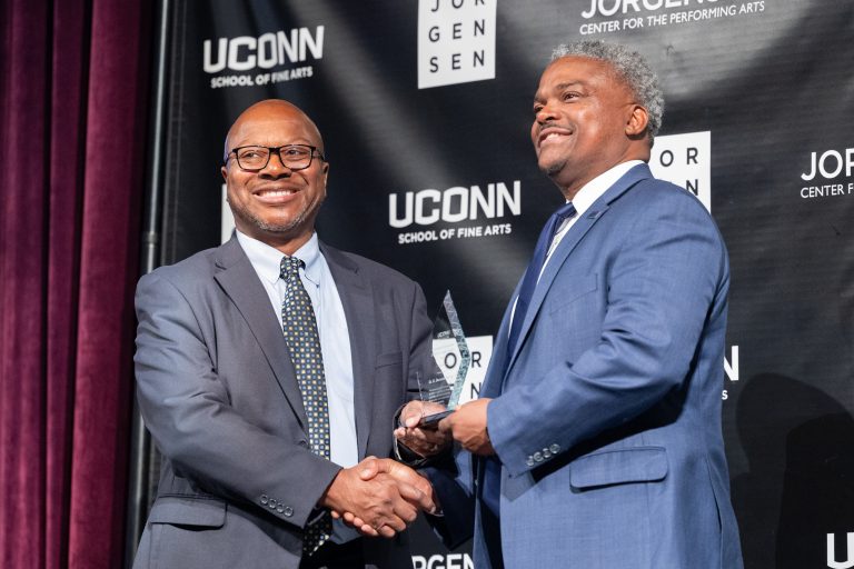 Two men in suits shaking hands as one presents an award to the other