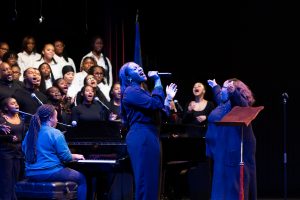 A large choir performing on stage with a soloist holding a microphone