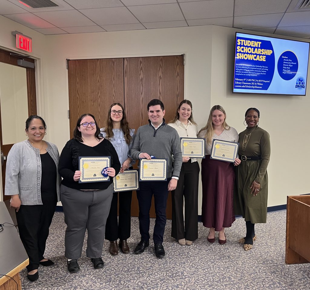Five UConn Law students hold certificates while standing with two law school administrators.