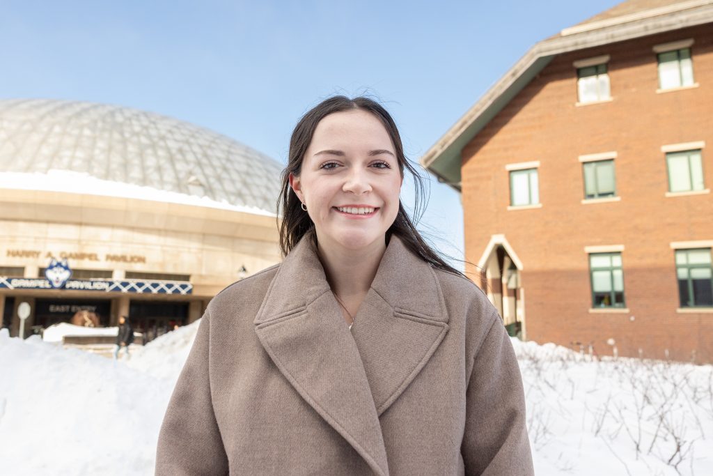 A young woman poses for a portrait photo with two large buildings in the background.
