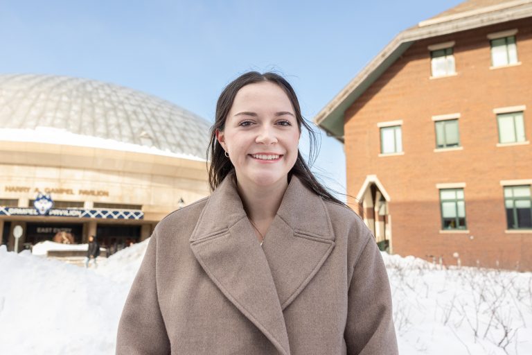 A young woman poses for a portrait photo with two large buildings in the background.