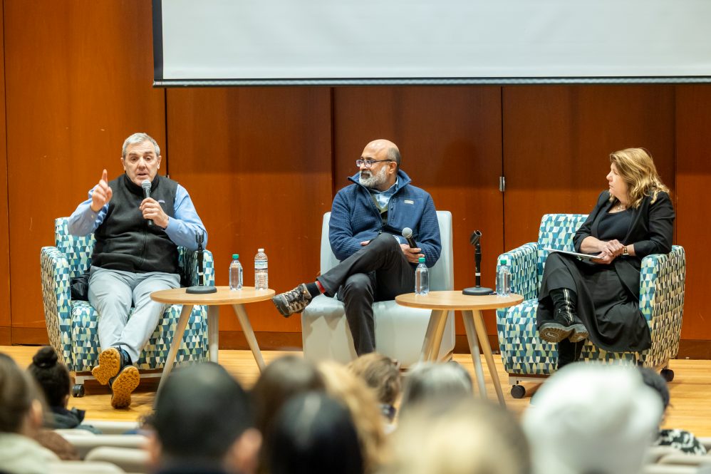 Three people sit in chairs on a stage