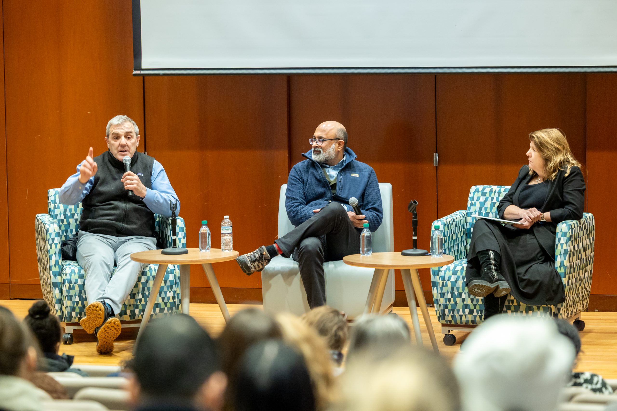 Three people sit in chairs on a stage