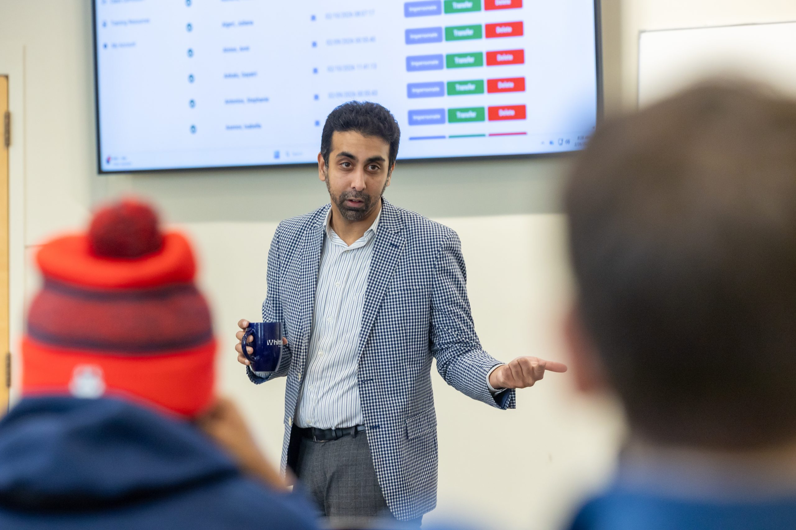 A university professor holding a coffee cup speaks to his class.
