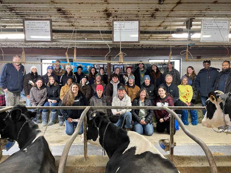 Students posing in a barn alongside the farm's owner and family.