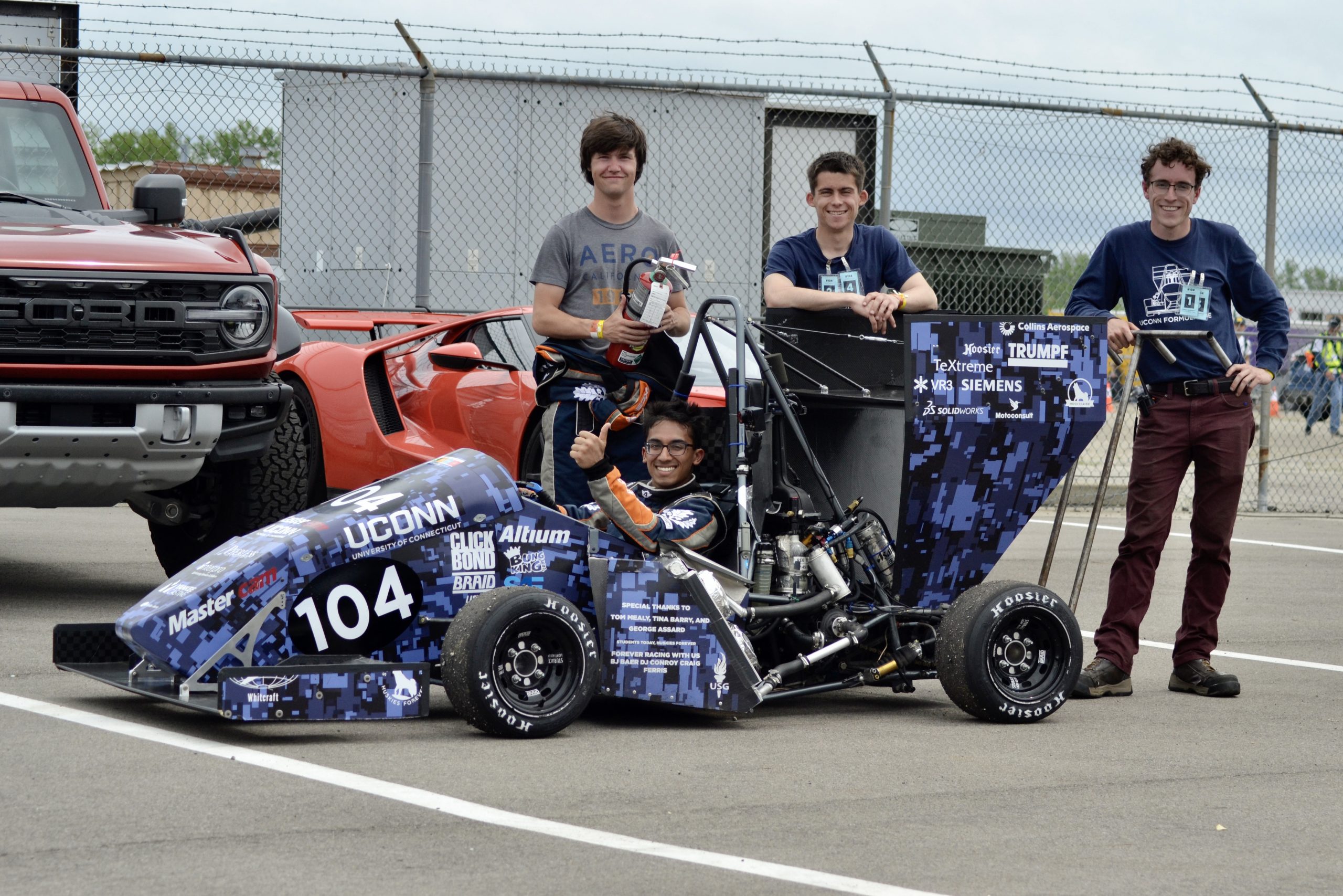 UConn Formula SAE students pose with a student-built race car at a competition track.