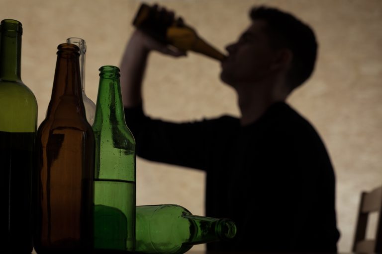Teenager drinking beer surrounded by beer bottles
