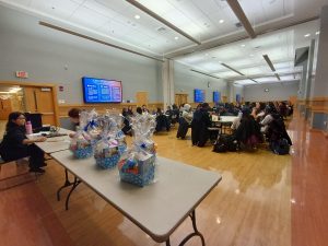 Bags of prizes sit on a table in the foreground while people play bingo in the background.