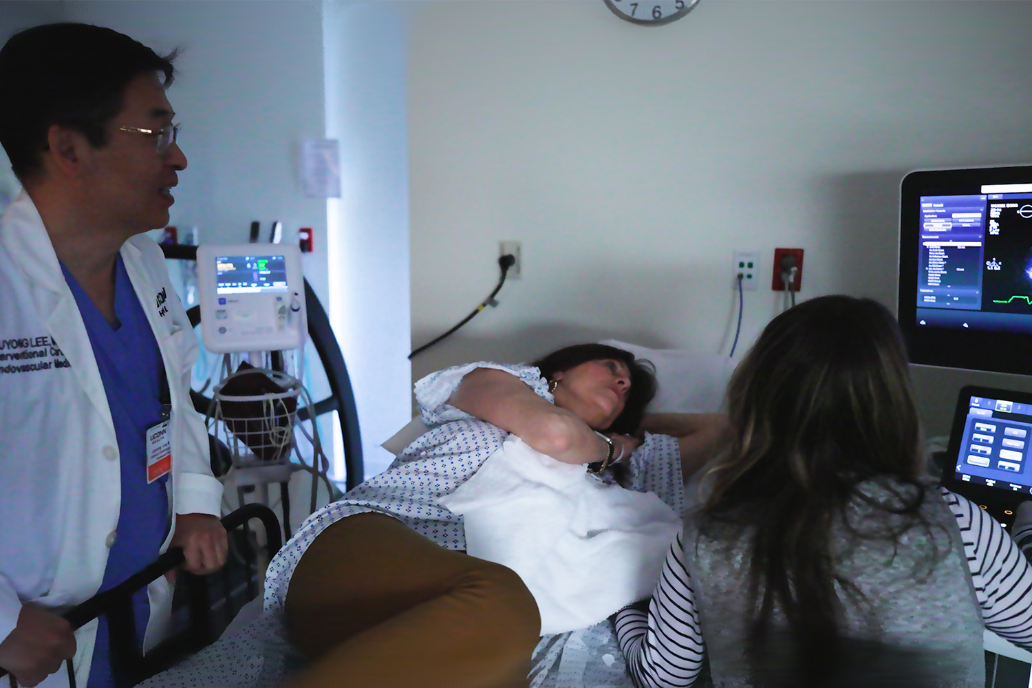 A patient laying in a bed while a doctor and an nurse stand around her looking at an ultrasound machine