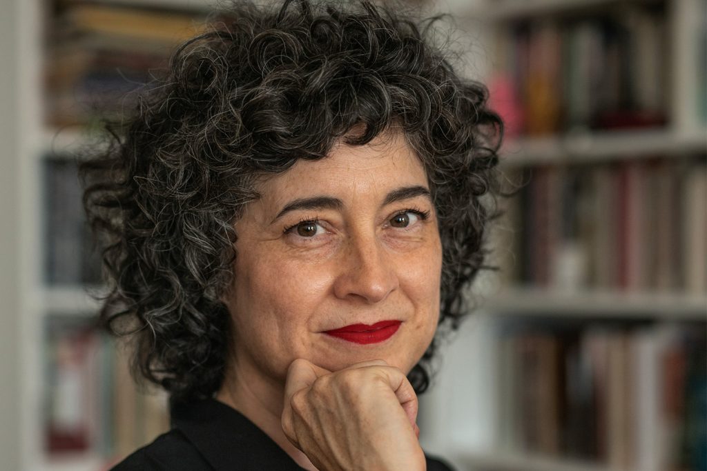 A woman with curly hair and red lipstick poses for a photo
