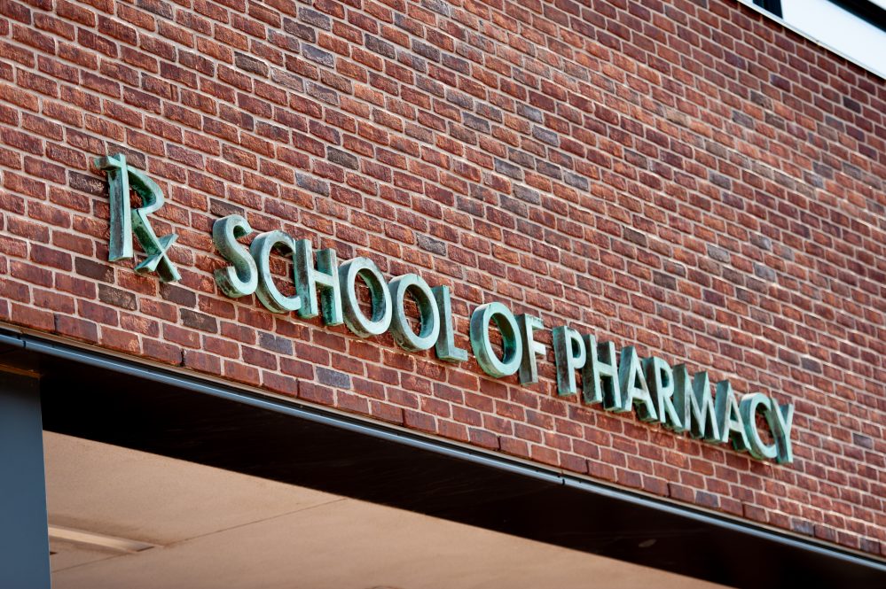The brick exterior of a building with the words School of Pharmacy in metal lettering