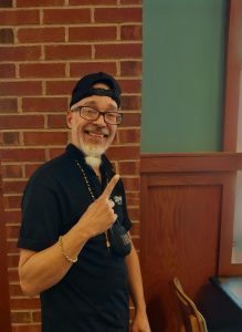 A man in blue holds his right hand up in the peace sign.