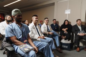 People in scrubs and white lab coats sitting together in a conference room.