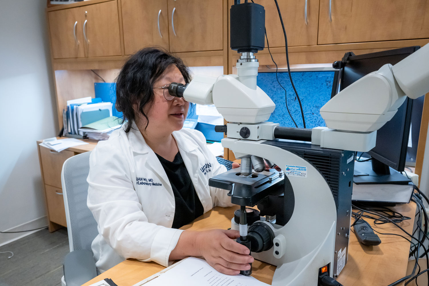 woman in lab coat looking into microscope