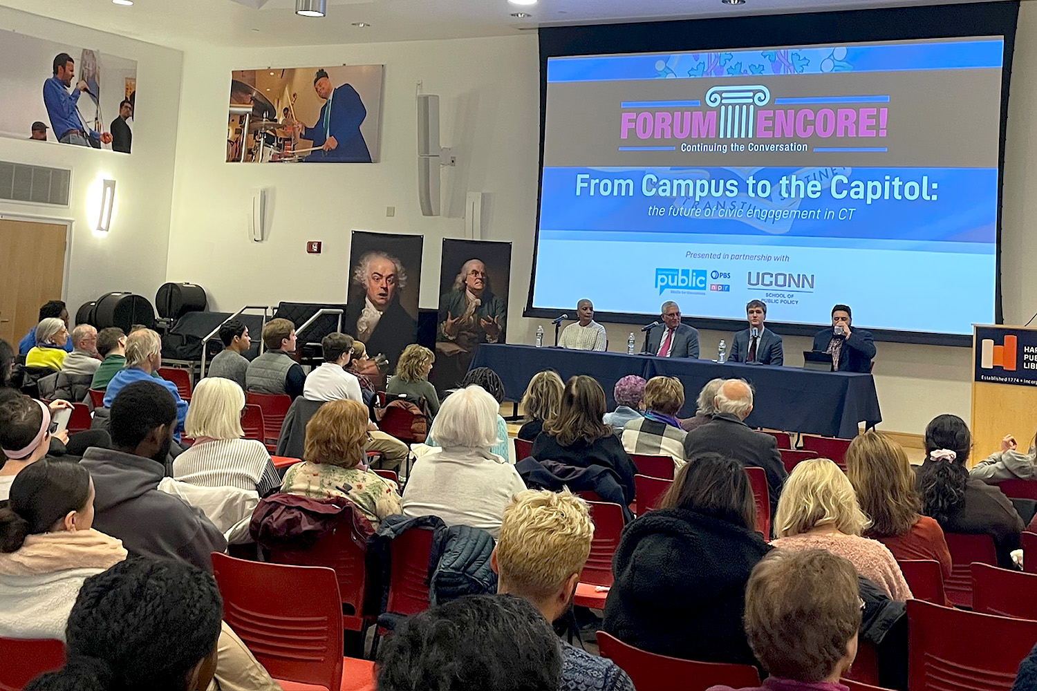 State leaders and a UConn student panelist speak on civic engagement in Connecticut as a packed audience looks on at the Hartford Public Library.