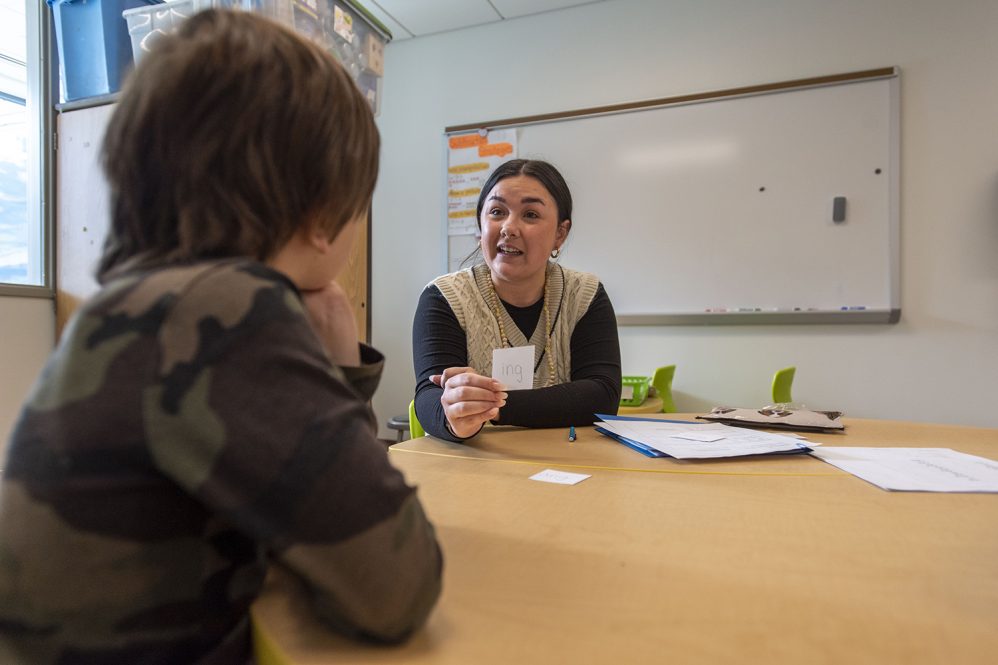 Female educator works with young male student at a desk.