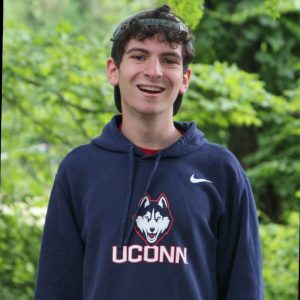 Alex Renzulli smiling in front of a tree-filled background, wearing a UConn sweatshirt