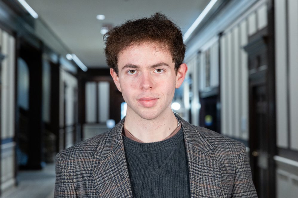 A man in a blazer stands inside a building for a portrait