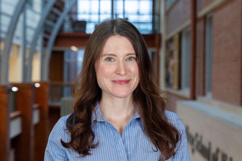 A woman with long brown hair in a blue shirt posing for a photo inside a building
