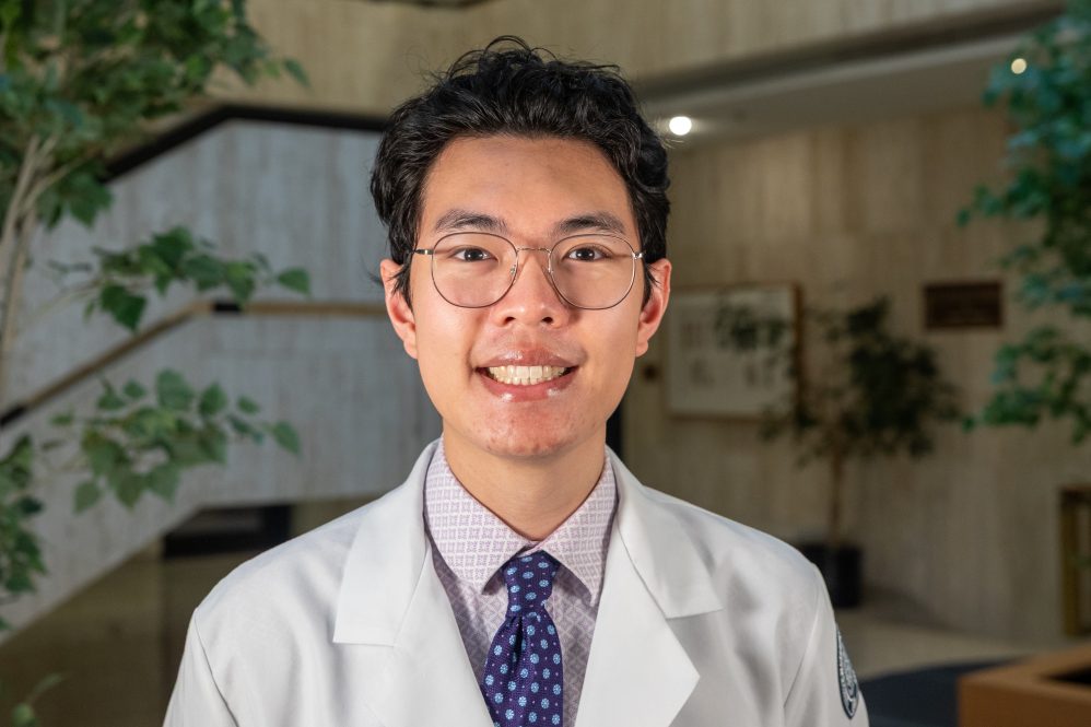 A man with glasses in a white doctors coat posing for a photo