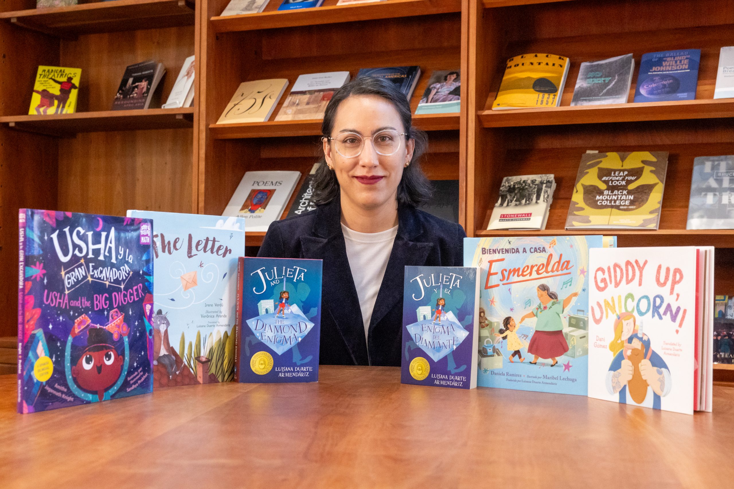 A woman poses at a table with six books.