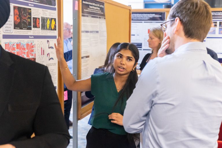 A young woman talks to a man whose back is turned to the camera while pointing at a poster showing her research.