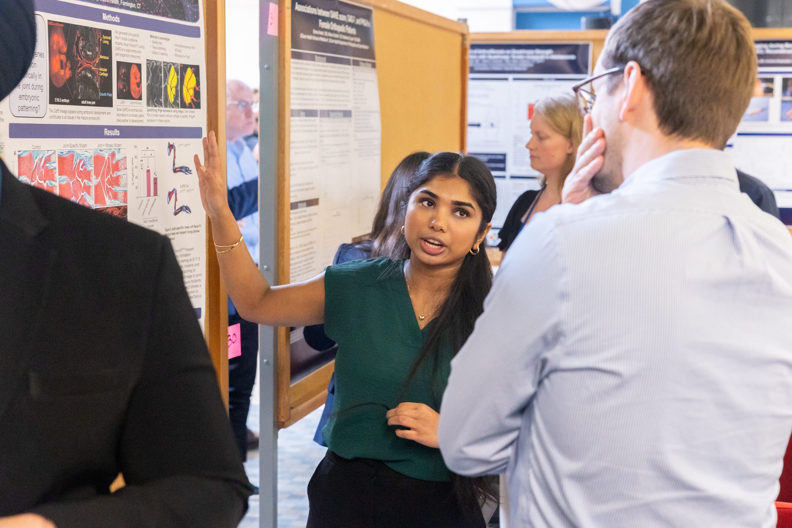 A young woman talks to a man whose back is turned to the camera while pointing at a poster showing her research.