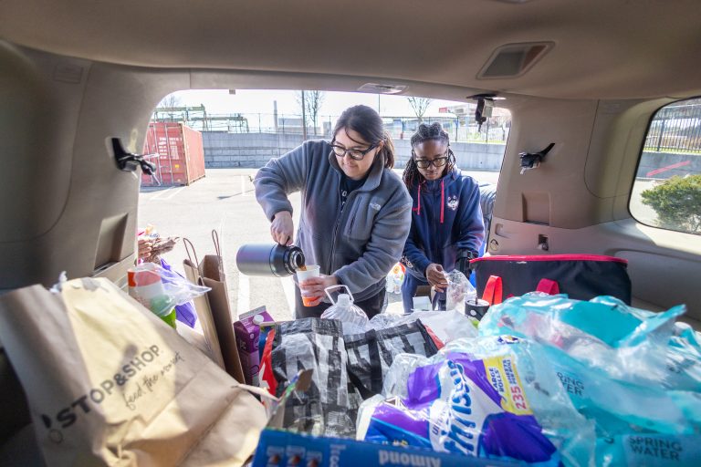 Two people load donated groceries and other supplies into the back of an SUV.