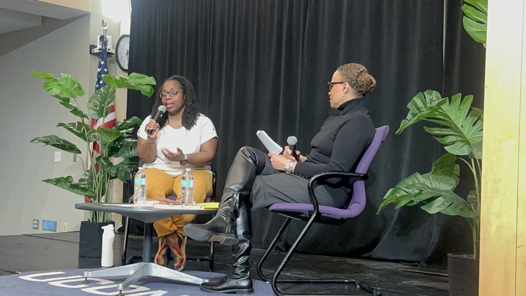 Two women sitting in chairs on a stage, having a conversation.