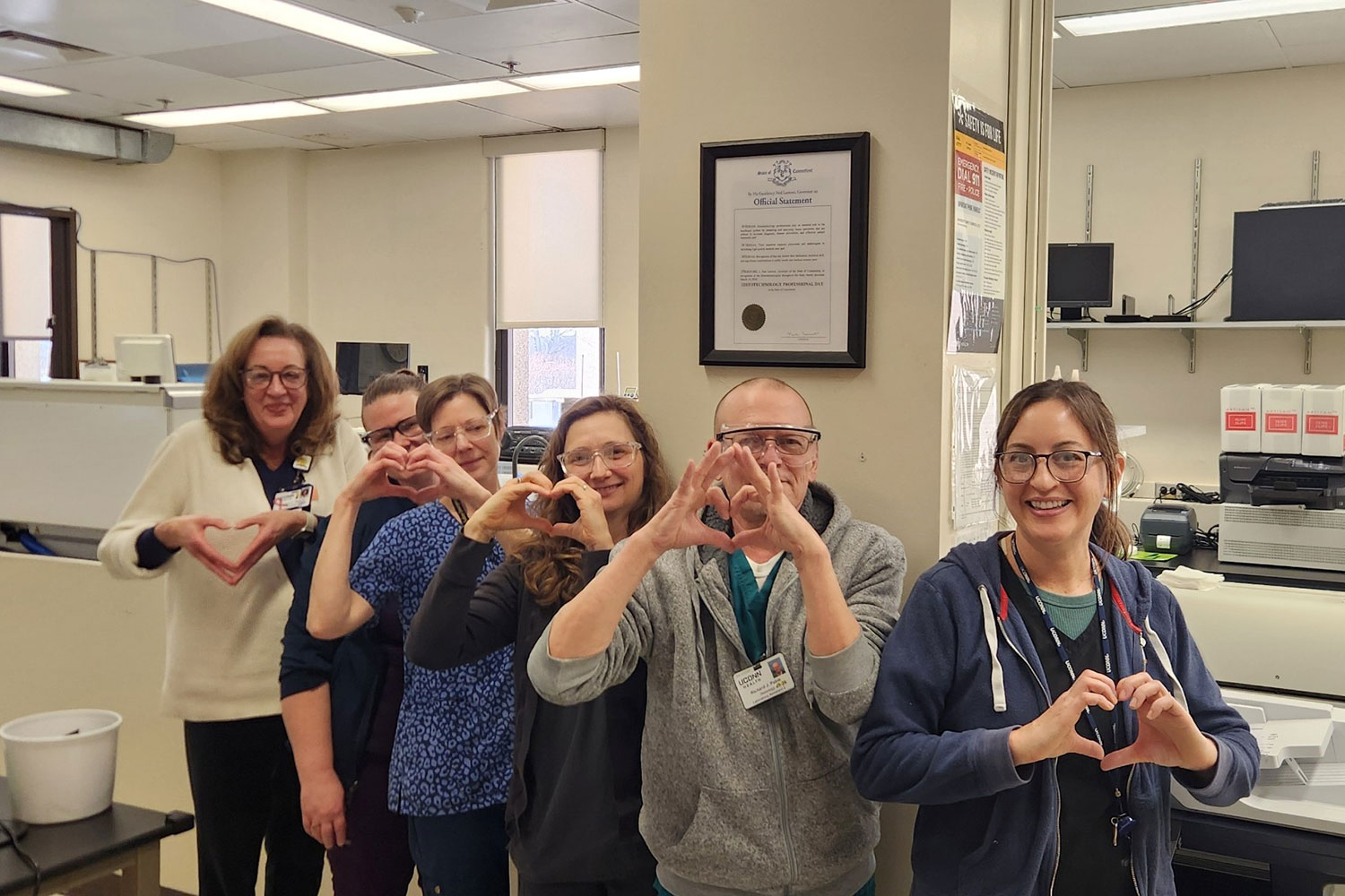 group portrait of six in pathology lab, Histotechnology Professionals Day proclamation hanging on wall behind them