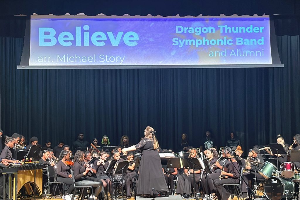 A woman conducts a high school band on a stage.