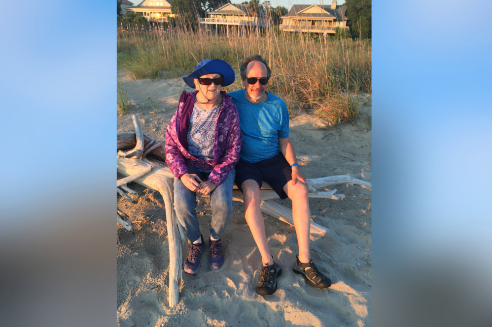 A woman and a man sitting on a rock at the beach