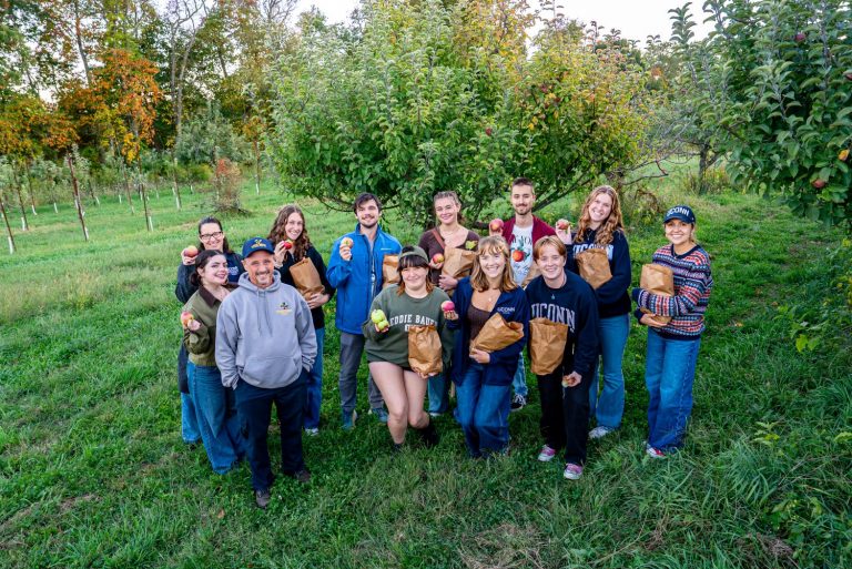 A group of students pose holding apples in an orchard
