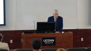 Ernesto Canalis addresses a large group from a speaker's rostrum with a UConn Health sign on the front.