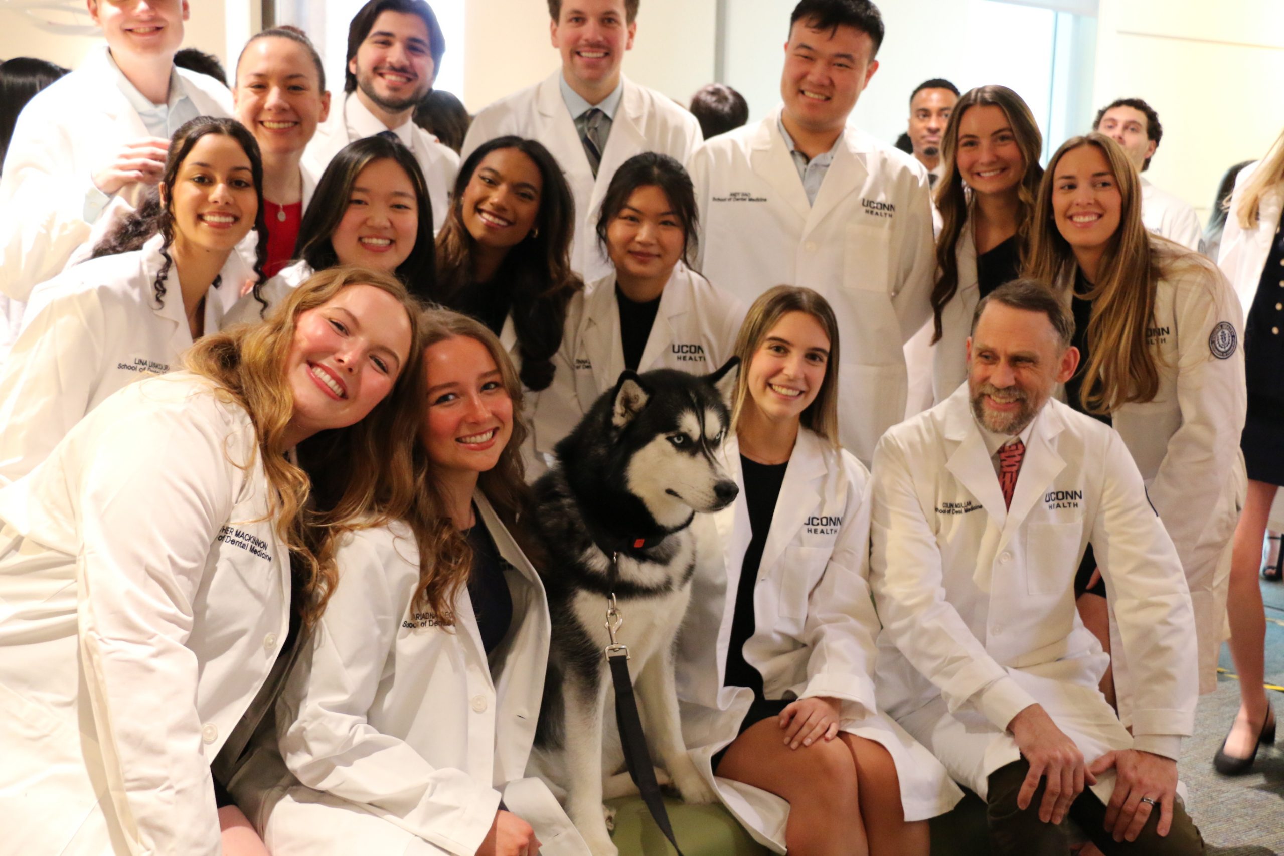 students in white coat pose with husky