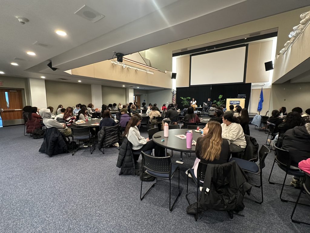 A large meeting room space full of tables at which people are sitting. 