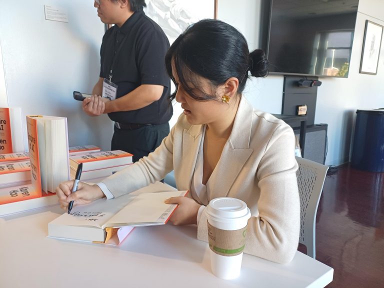 A woman signing a book at a table with coffee