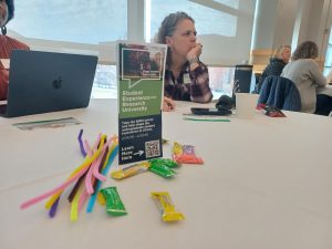 A photo of the survey handout on a table with a woman in the background and candy and pipe cleaners next to it