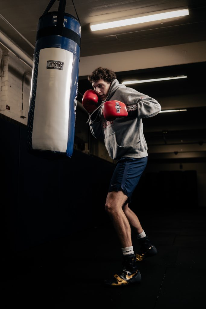 A young man in boxing gloves, about to start practicing with a heavy bag.
