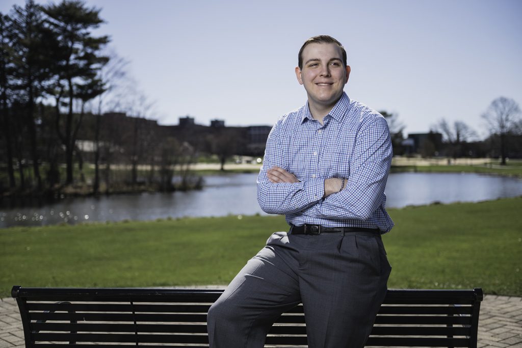 A student in businesswear poses confidently in front of Mirror Lake