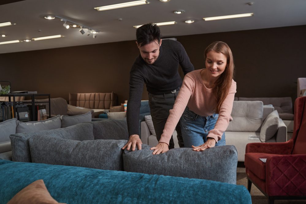 A man and woman in a furniture store examine a couch together.