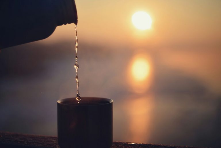 Water being poured into a cup with the sun in the background