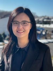 A woman wearing dark professional clothes and glasses smiling for a photo outdoors