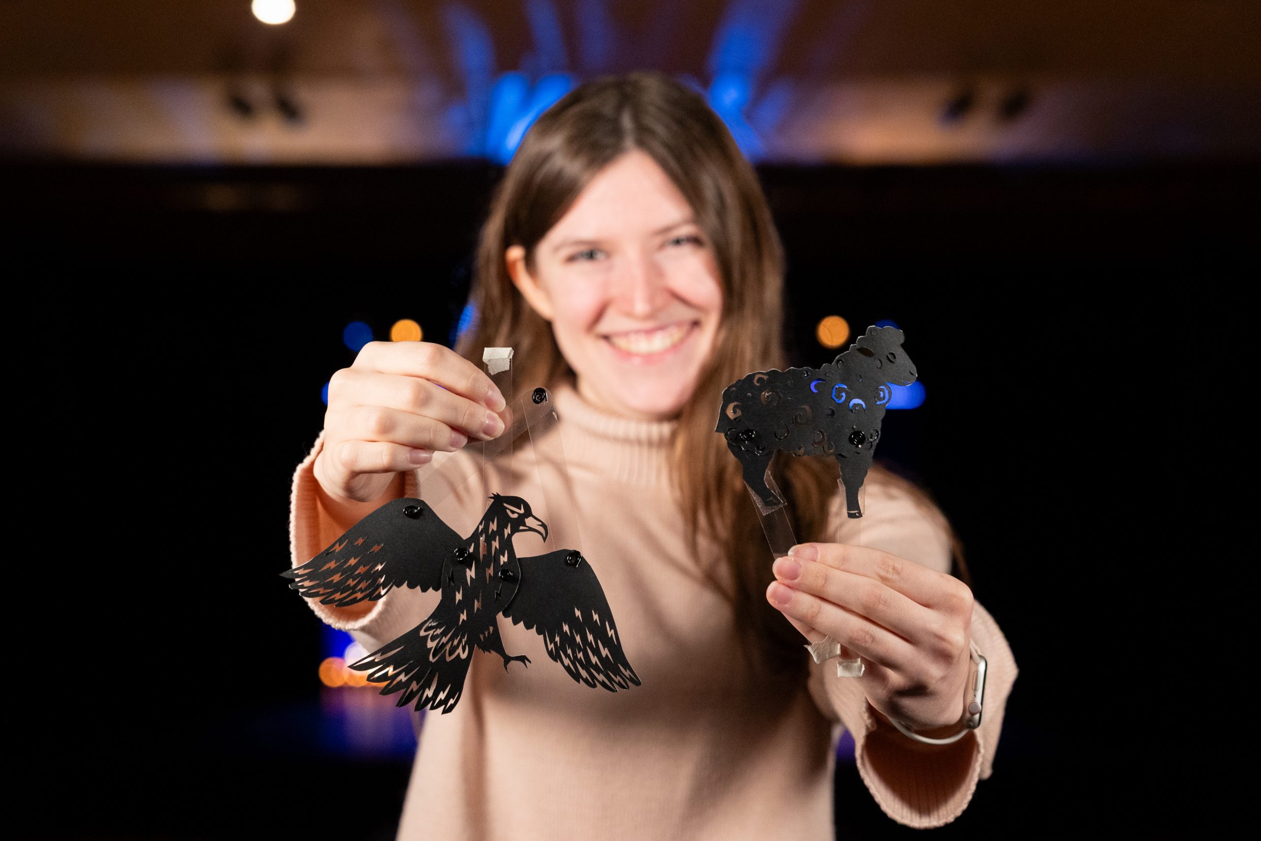 A woman holding out two puppets of a bird and a sheep