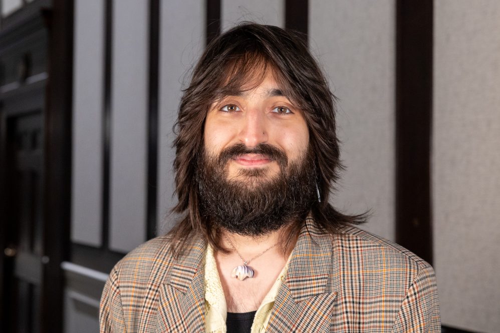 A man with a beard poses for a photo in a hallway