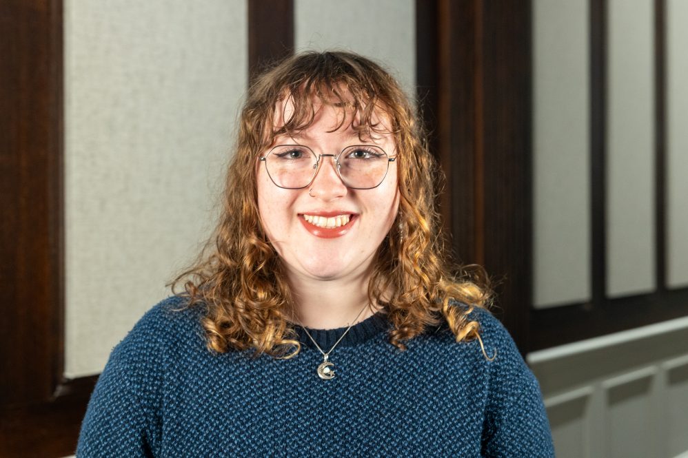A woman with glasses poses for a photo inside a hallway