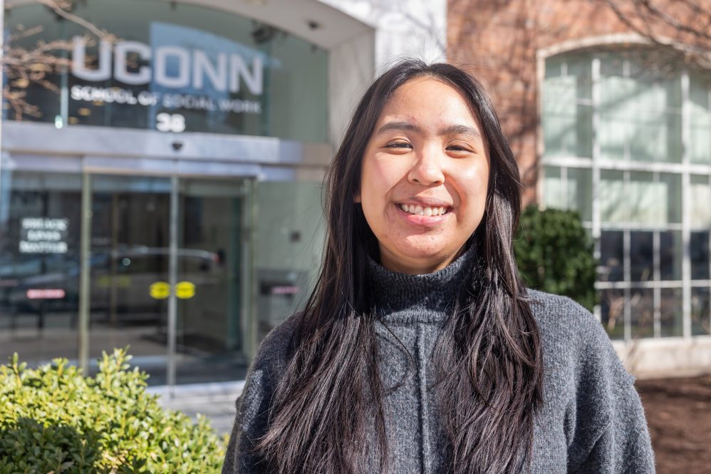 A woman with long brown hair posing for a photo outside the UConn School of Social Work