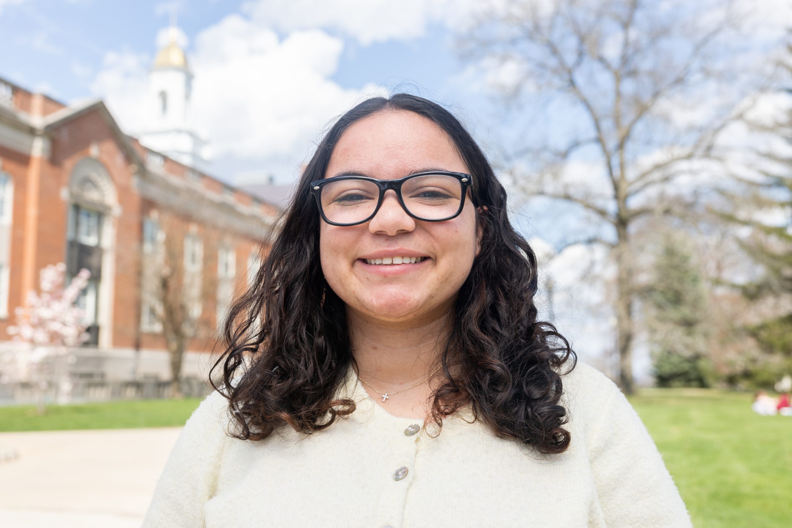 A woman with glasses poses for a photo outside a building on a spring day