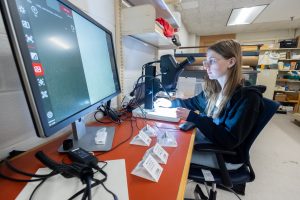 A woman in glasses looks through a microscope