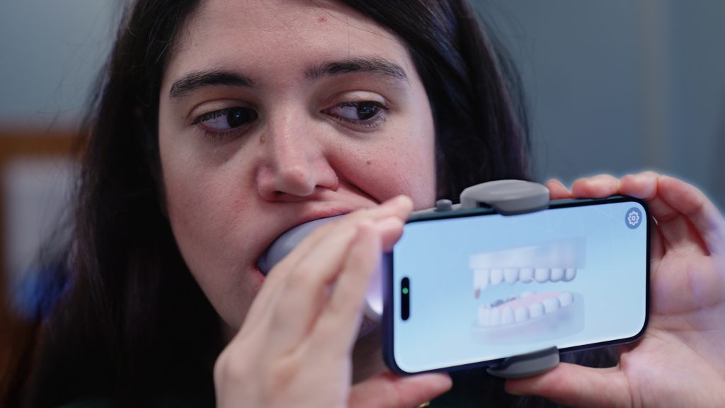 A mock patient demonstrates using a scan box and her cell phone how AI is being used in orthodontics. (Ryan Bernat/UConn Health)